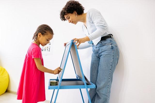 Child writing on board with teacher